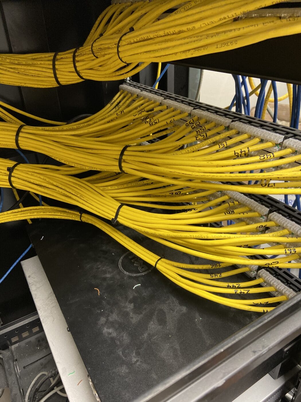 Several neatly organized yellow network cables, part of structured network cabling services, are bundled and connected to a server rack, with a black Dell device underneath them.